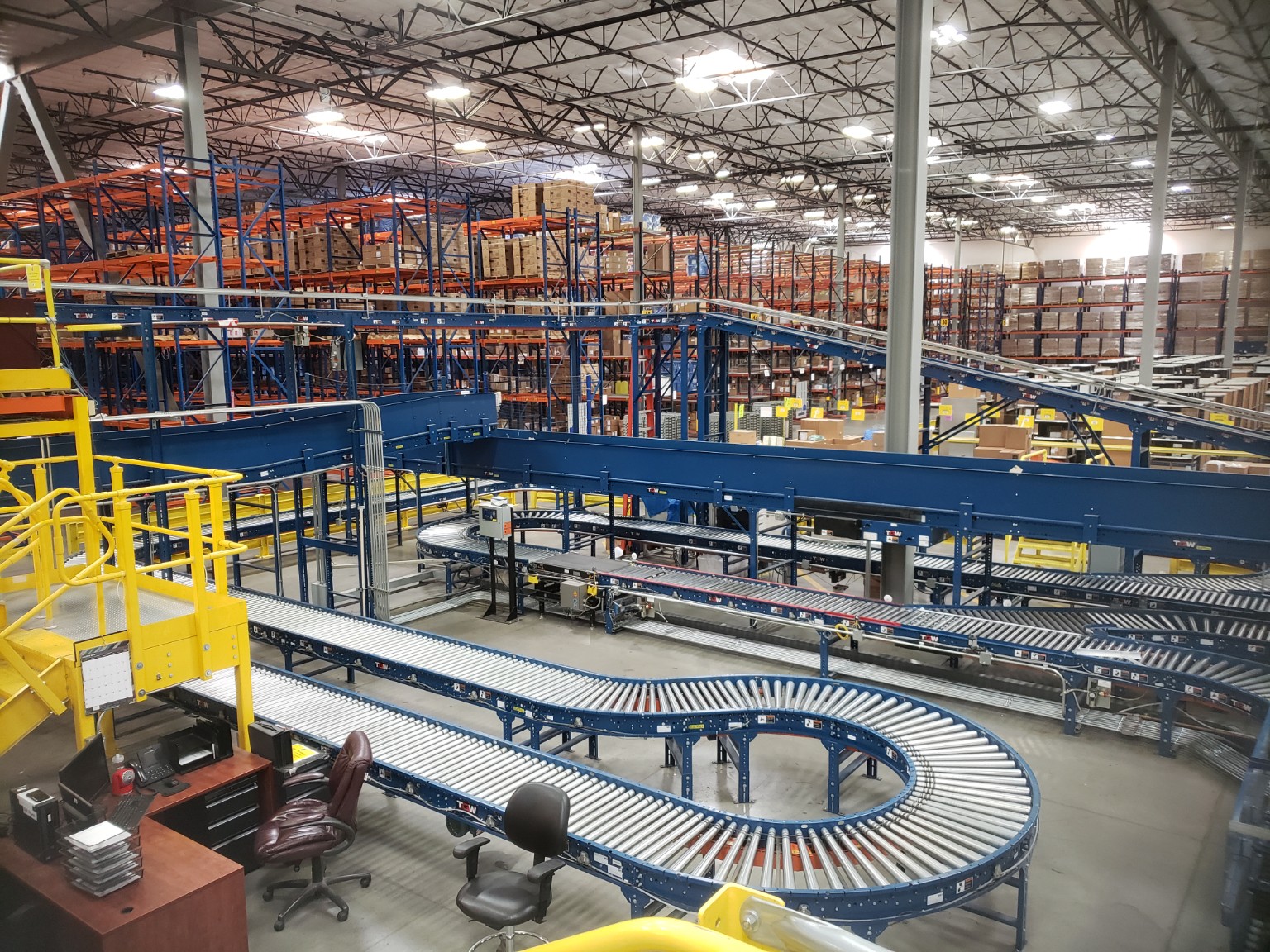 Large warehouse conveyor system with elevated runs, curves, and pallet racking