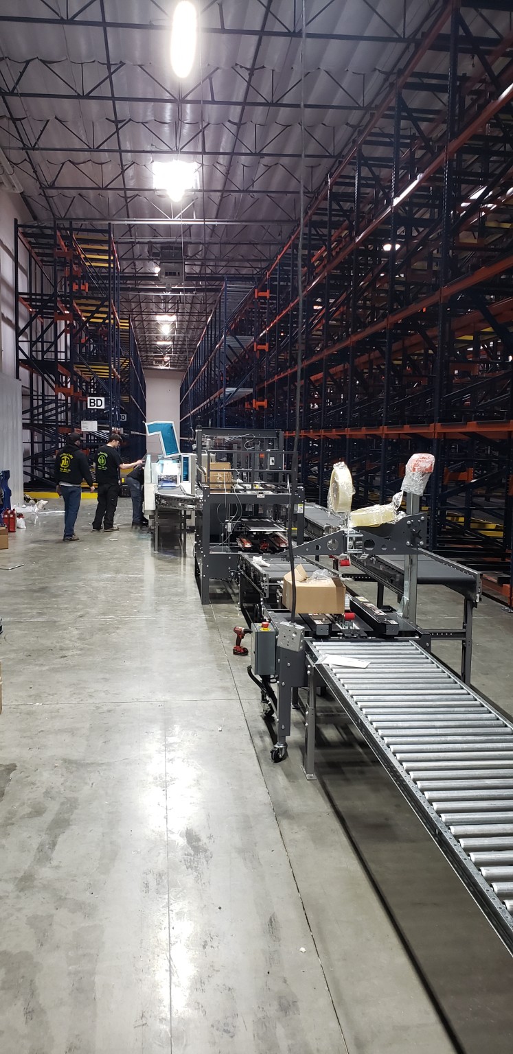 Conveyor and packaging equipment installation between pallet rack aisles